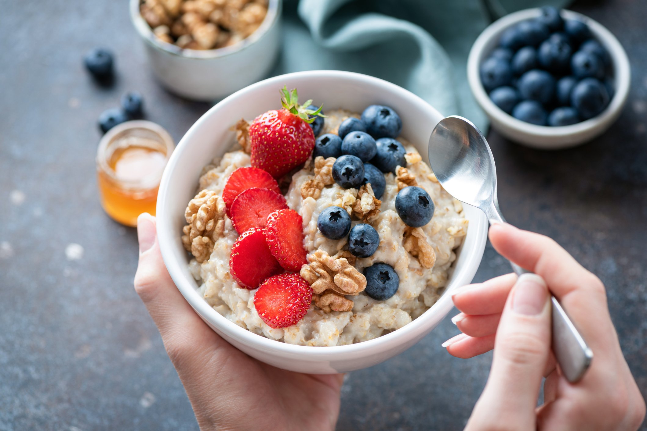 Person holds a bowl of oatmeal with berries and walnuts.